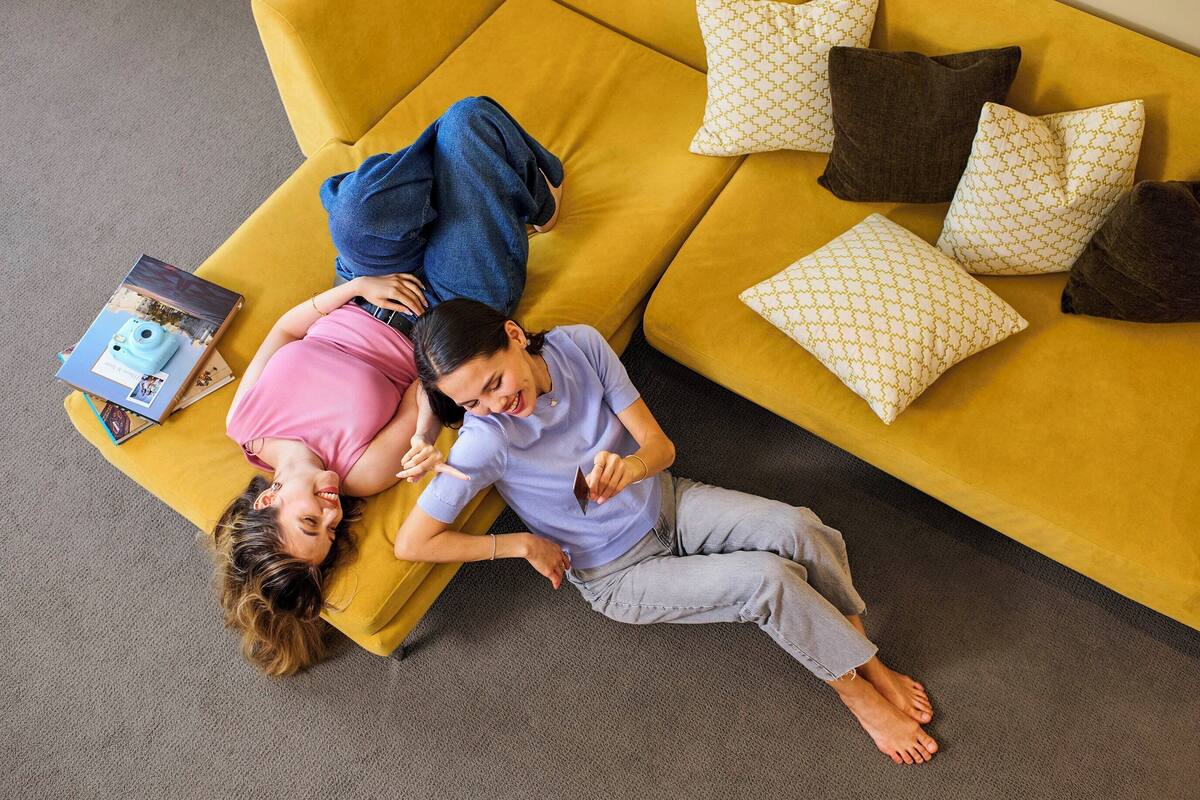 Two people lying on a yellow sofa with a book and a camera on it.
