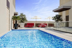 A swimming pool with a tiled edge, red lounge chairs, and umbrellas. - Centro Capital Doha By Rotana (Doha)