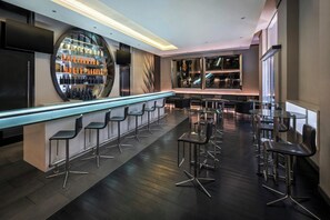 A modern bar area with a long counter, multiple stools, and a variety of bottles. - Centro Capital Doha By Rotana (Doha)