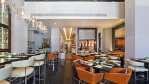 Um restaurante moderno com pé-direito alto, iluminação pendente e um corredor central.