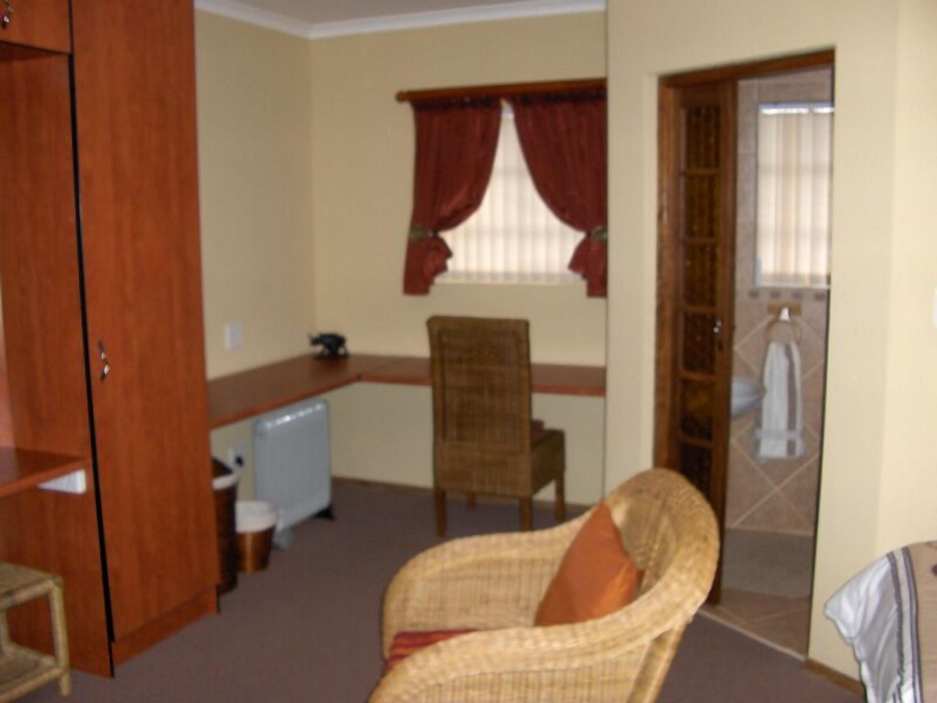 A room with a wooden desk, a wicker chair, a small table, and a wardrobe.
