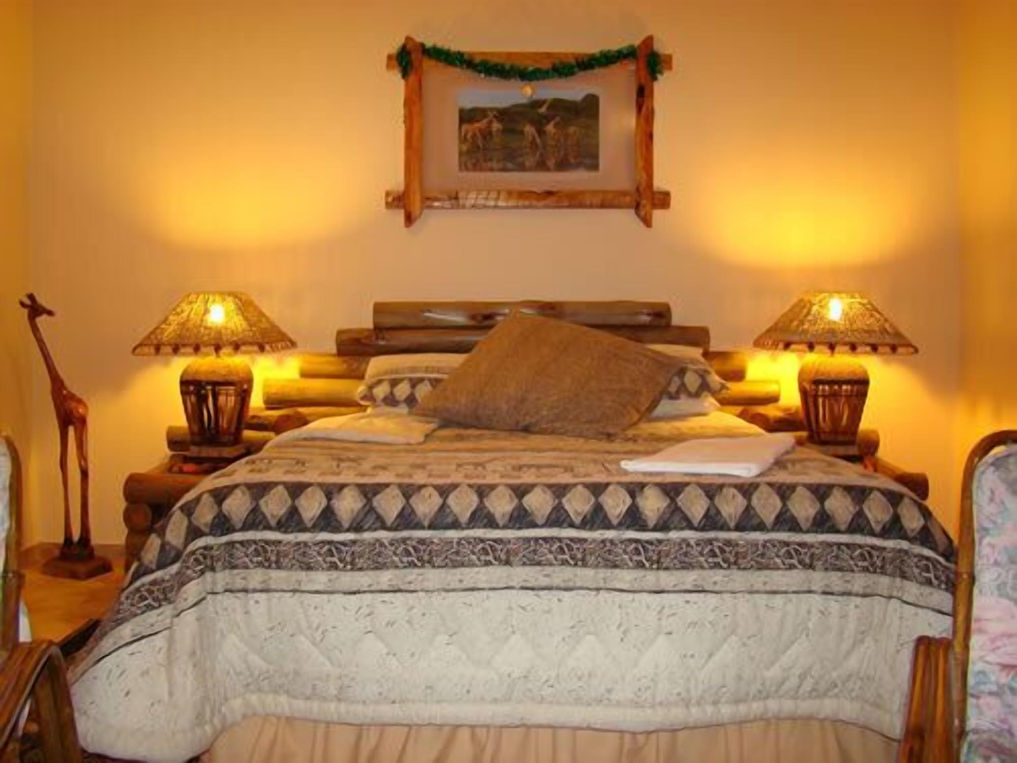Uma cama com um cobreleita estampado, duas luminárias, um quadro na parede e uma estátua de girafa ao lado da cama.