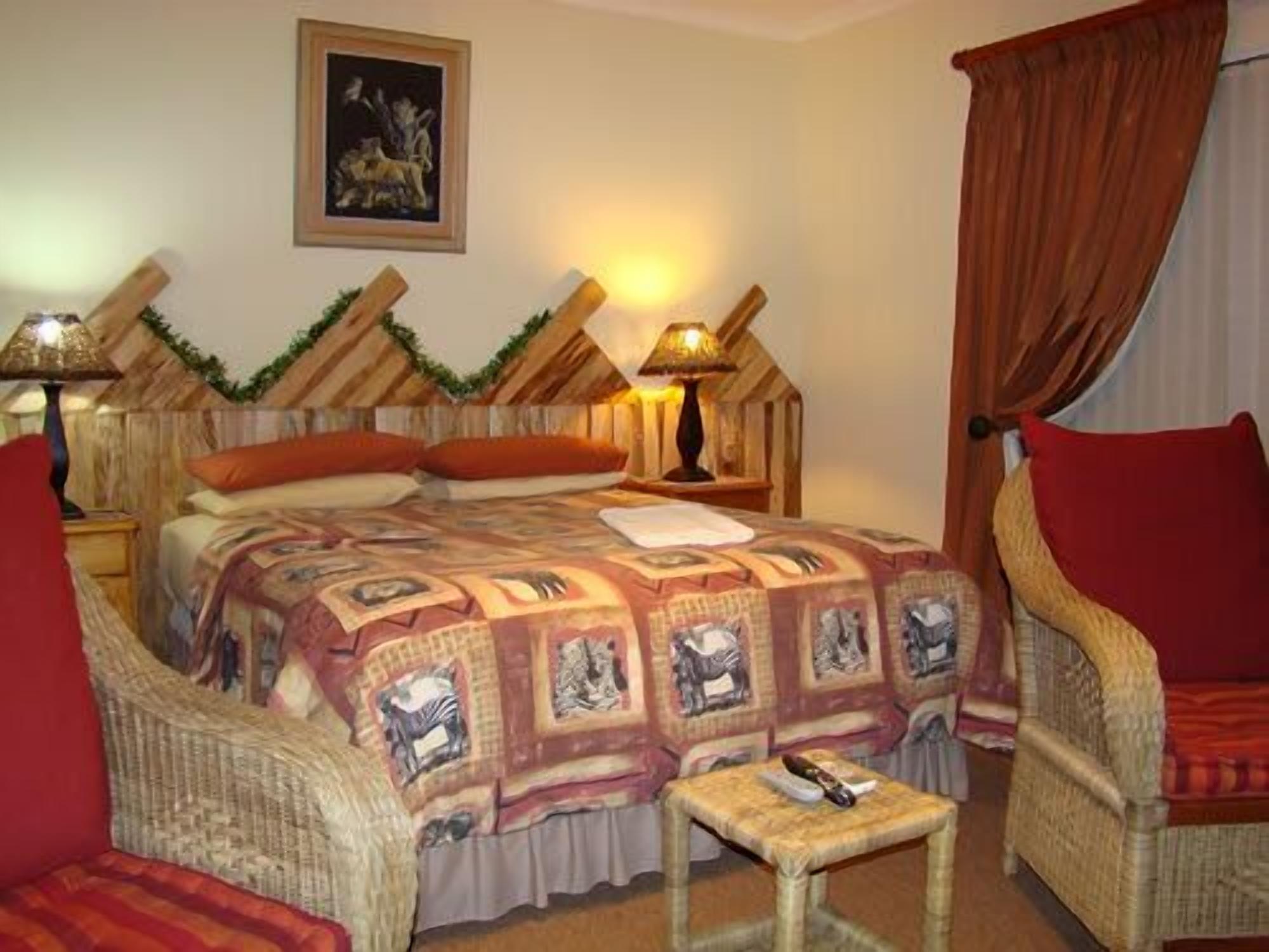 Una habitación acogedora con una cama, dos sillones de mimbre, una mesita y una lámpara.