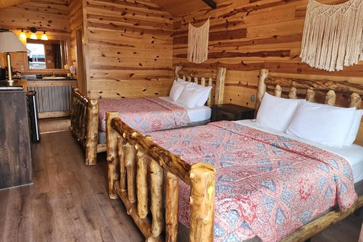 Quarto de cabana de madeira com duas camas, uma cabeceira de madeira e uma pequena cozinha.