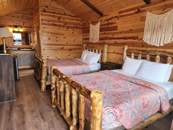 A wooden cabin room with two beds, a wooden headboard, and a small kitchenette.