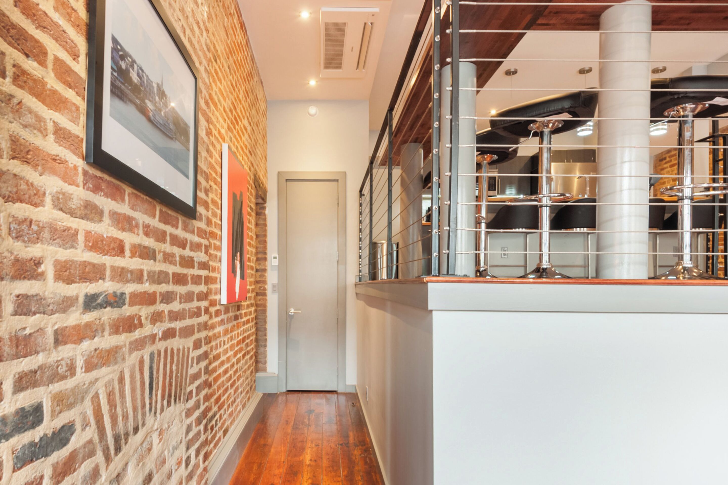 A narrow hallway with a brick wall on one side and a white counter with kitchen equipment on the other.