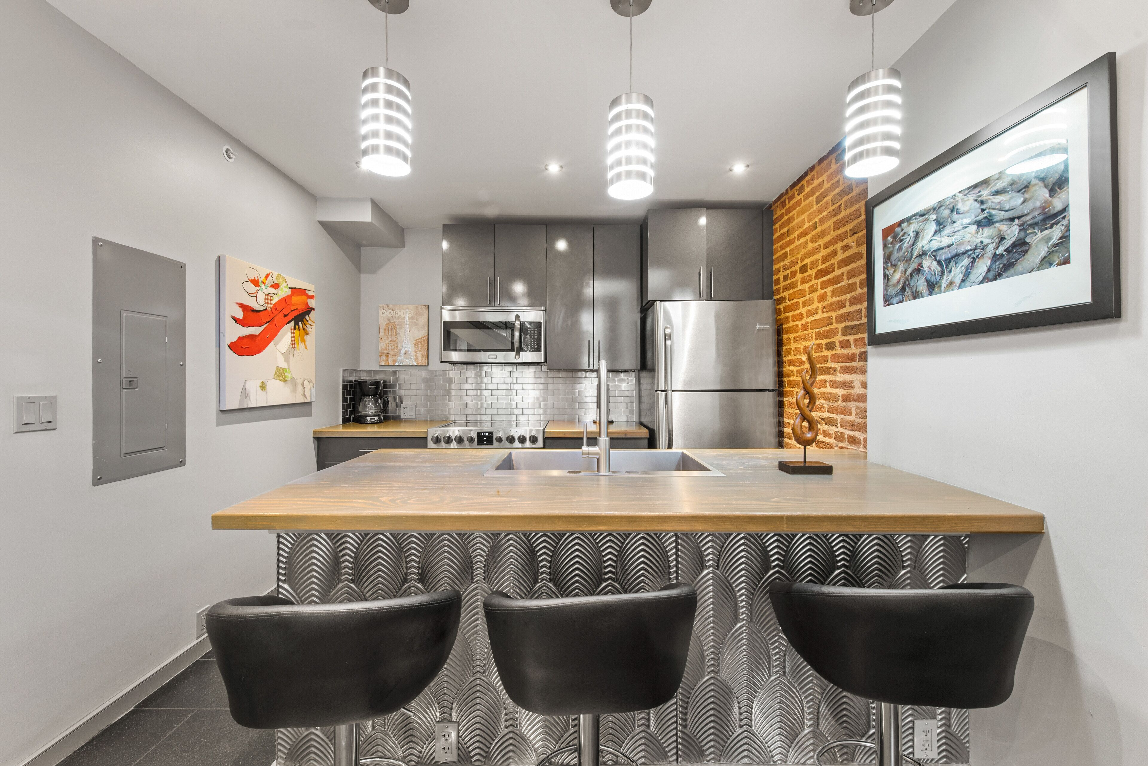 Een moderne keuken met een centraal eiland, roestvrijstalen apparatuur en zwarte barkrukken.
