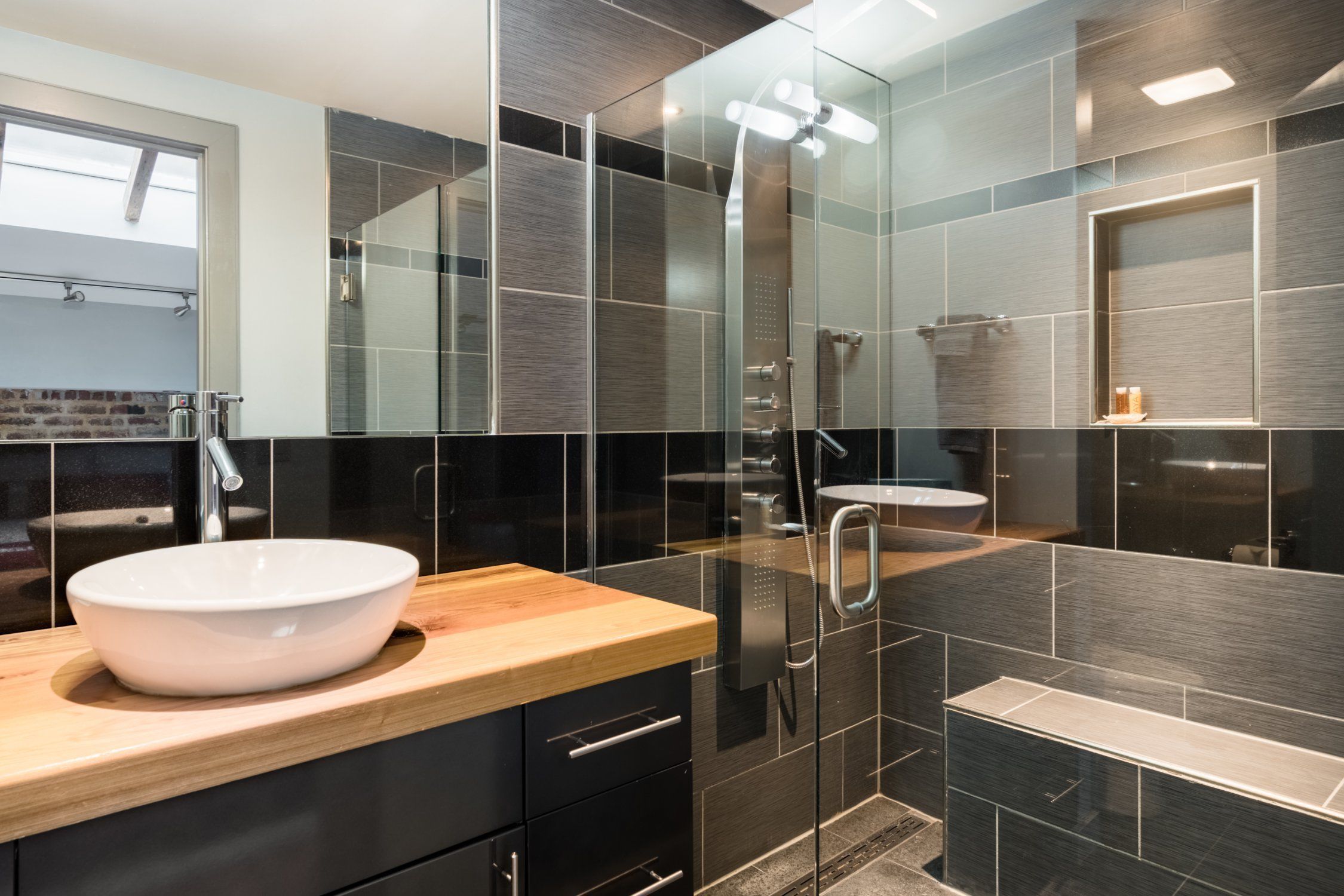 Een moderne badkamer met een groot wit wastafelblad, een douchecabine van glas en een houten aanrecht.