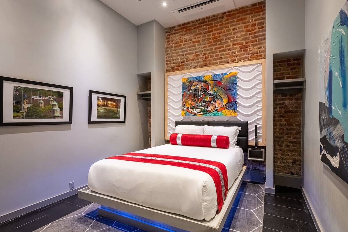 A modern hotel room with a bed, a brick accent wall, and artwork on the walls.
