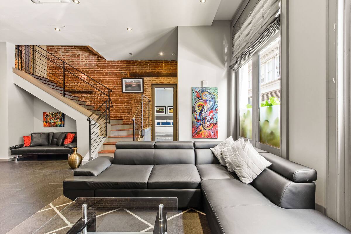 A modern living room with a sectional sofa, a staircase, and large windows.