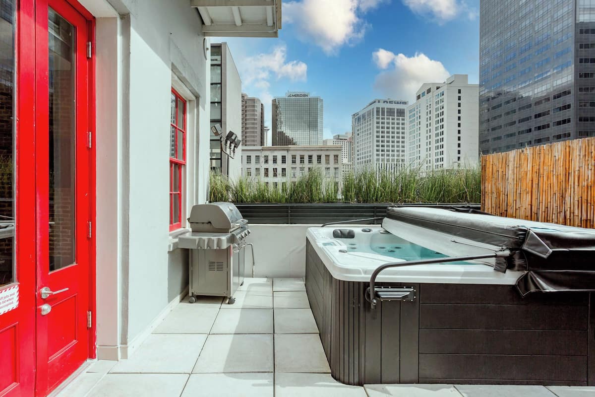 A rooftop patio with a hot tub, a grill, and a red door.
