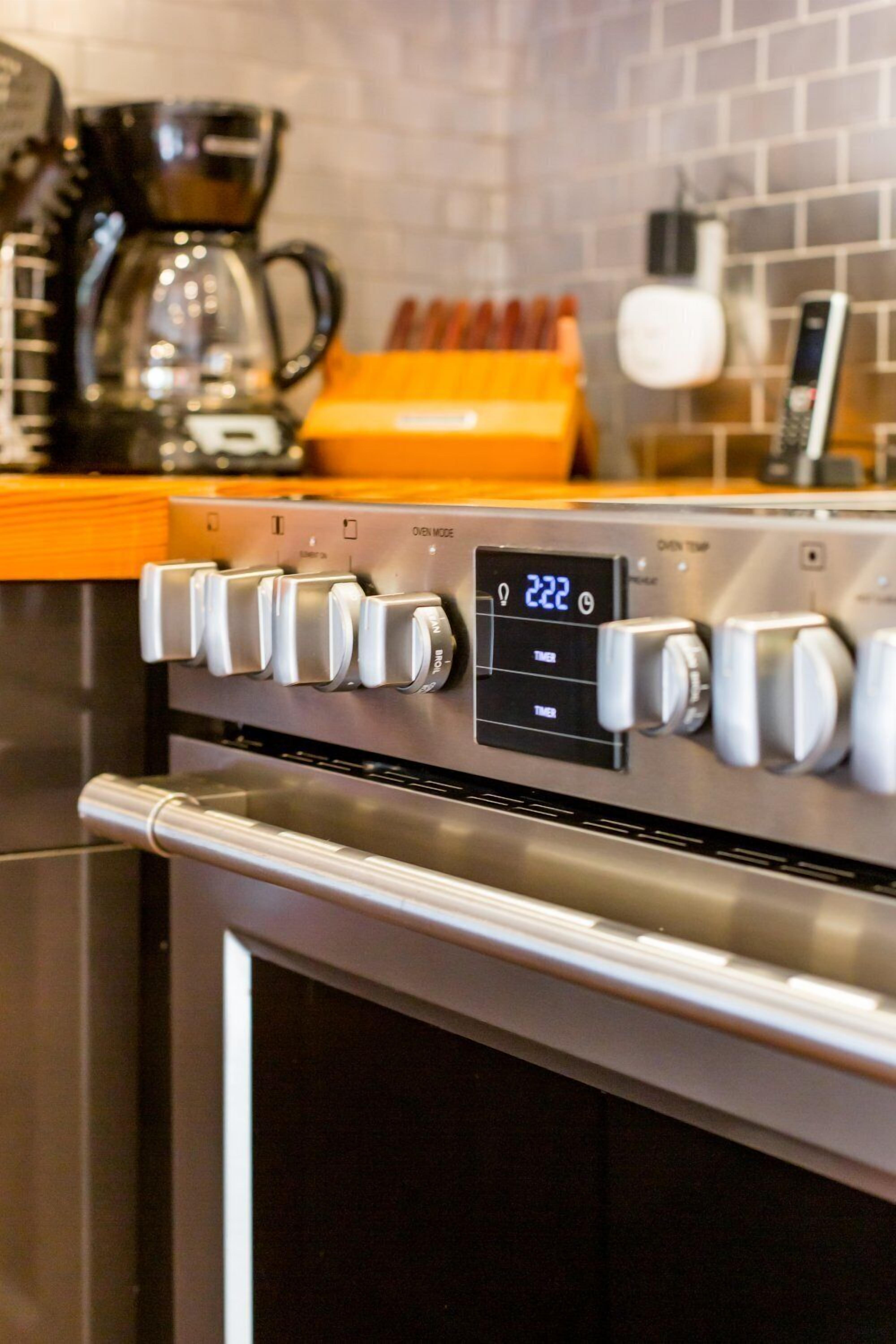 A kitchen with a stainless steel oven, a digital clock displaying 22:22, and a coffee maker.