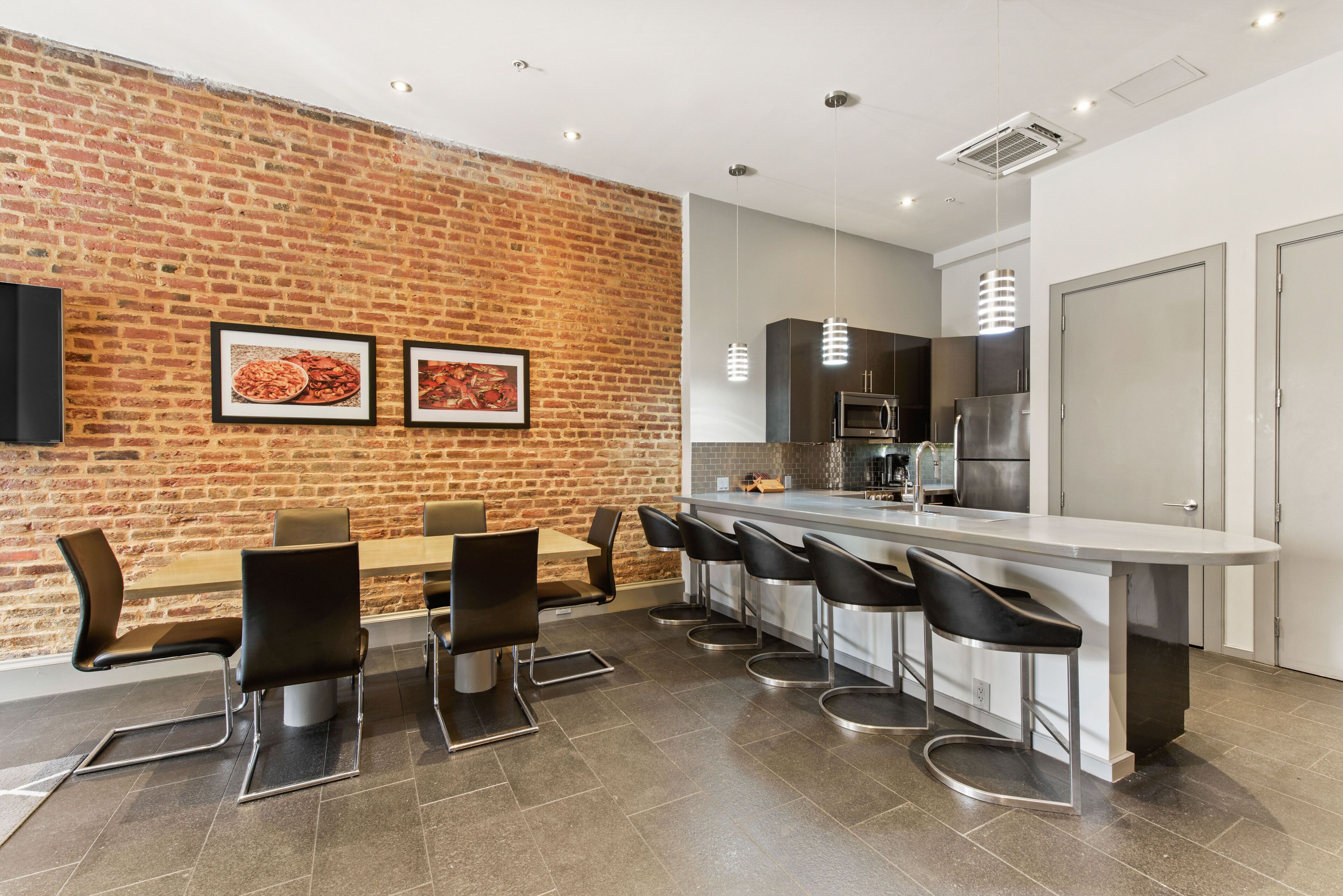 A modern kitchen with a brick wall, a long dining table, and bar stools.