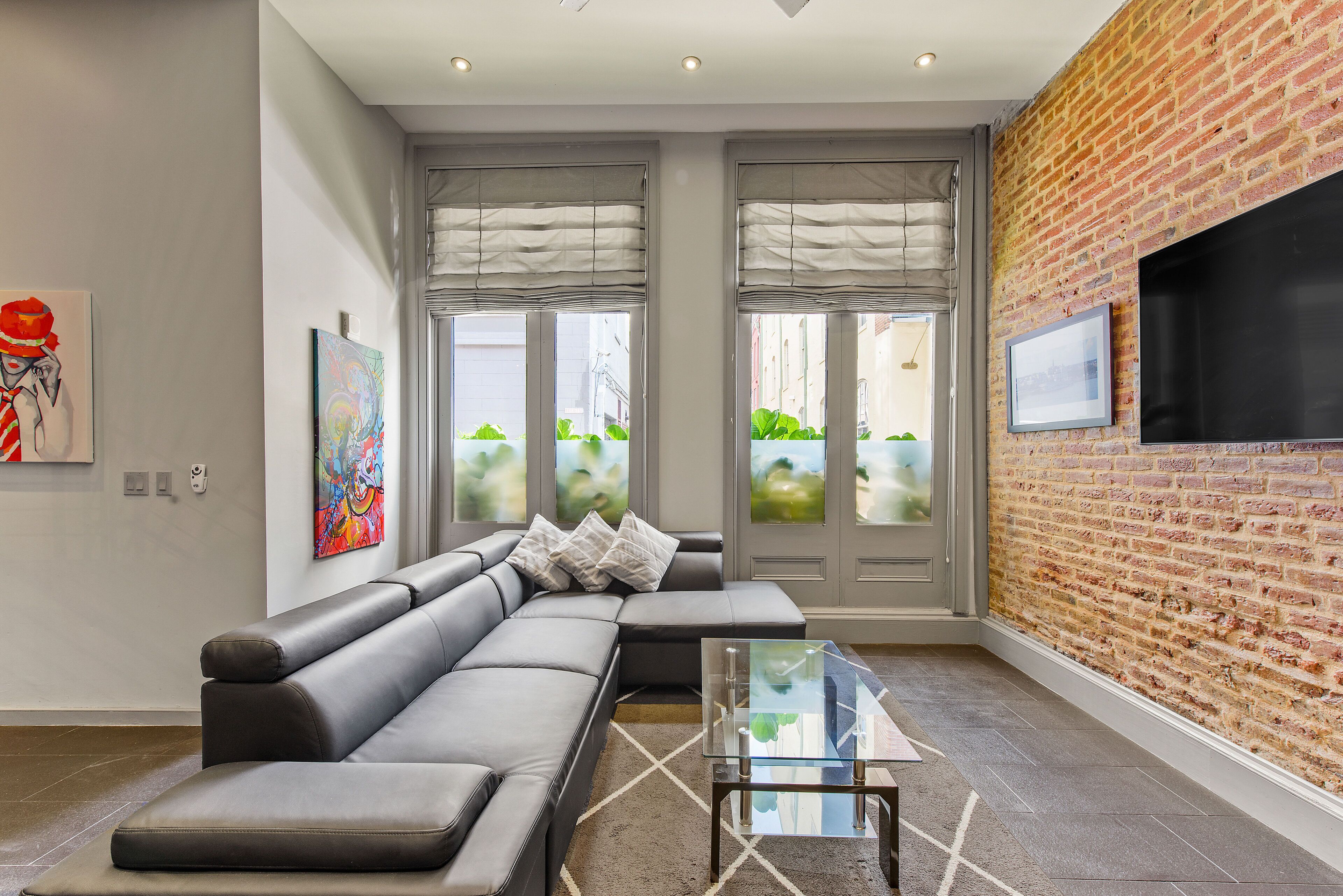 A modern living room with a sectional sofa, a glass coffee table, and a brick wall.