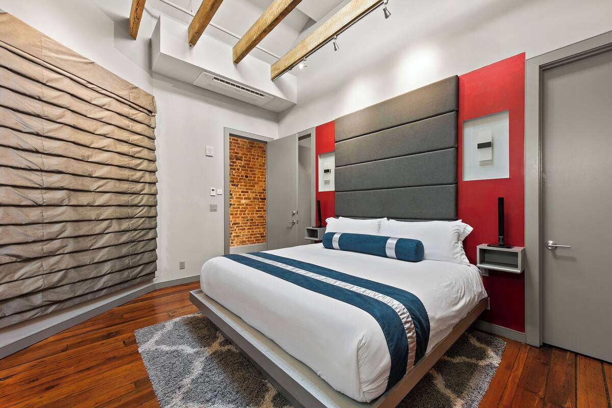 A modern bedroom with a large bed, a brick wall, and a red accent wall.