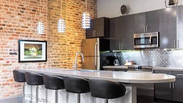 Une cuisine moderne avec un mur en briques, des appareils électroménagers en acier inoxydable et un îlot central doté de tabourets de bar.