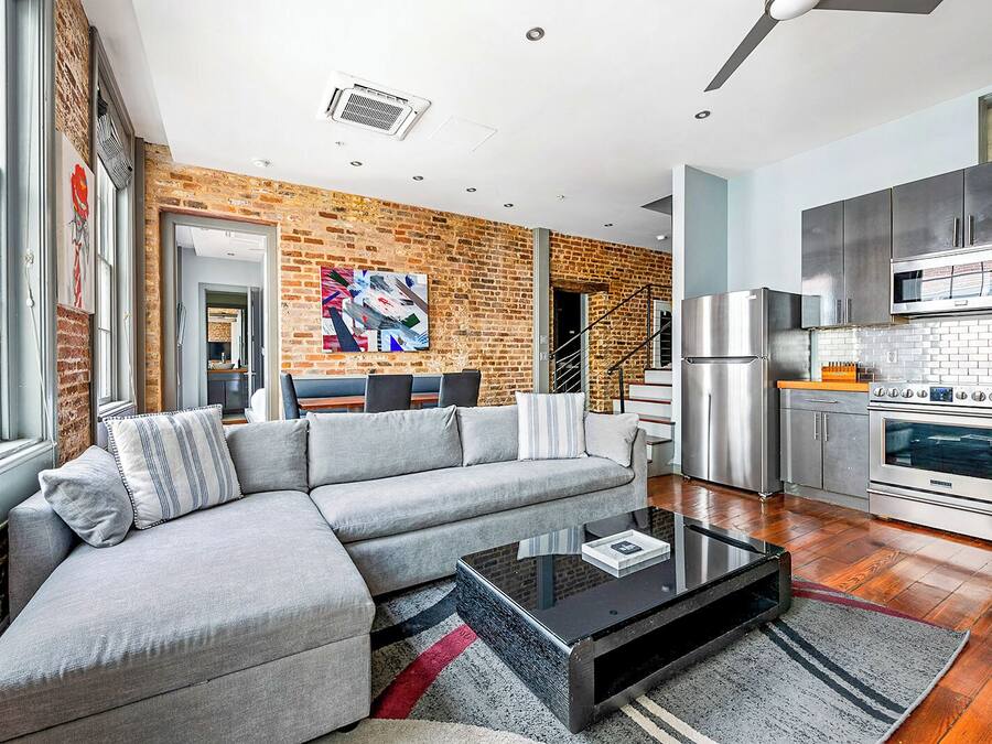 A modern living room with a grey sectional sofa, a black coffee table, and a brick wall.