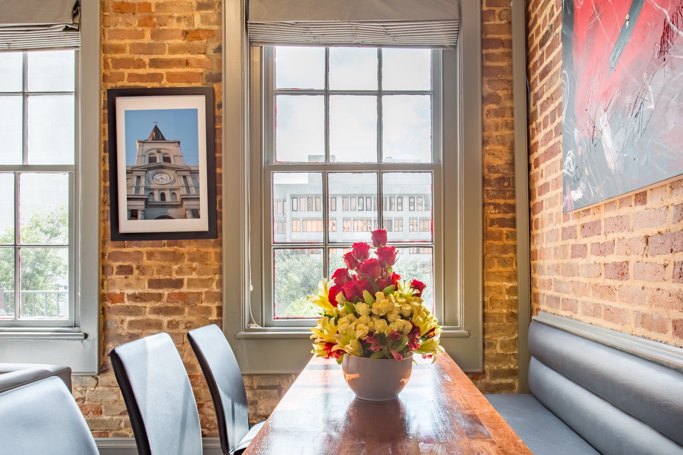 A dining area with a wooden table, cushioned bench seating, and a large window with a view of buildings.