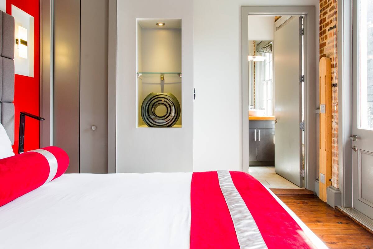 A hotel room with a bed, a red and white striped bedspread, a circular artwork on the wall, and a view into the kitchen area.