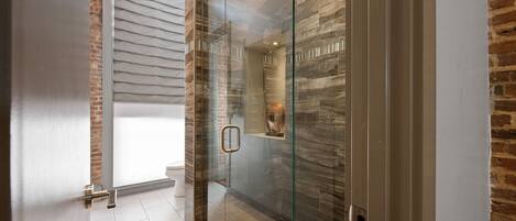 Un baño moderno con ducha de vidrio, inodoro a la vista y pared decorativa de ladrillo.
