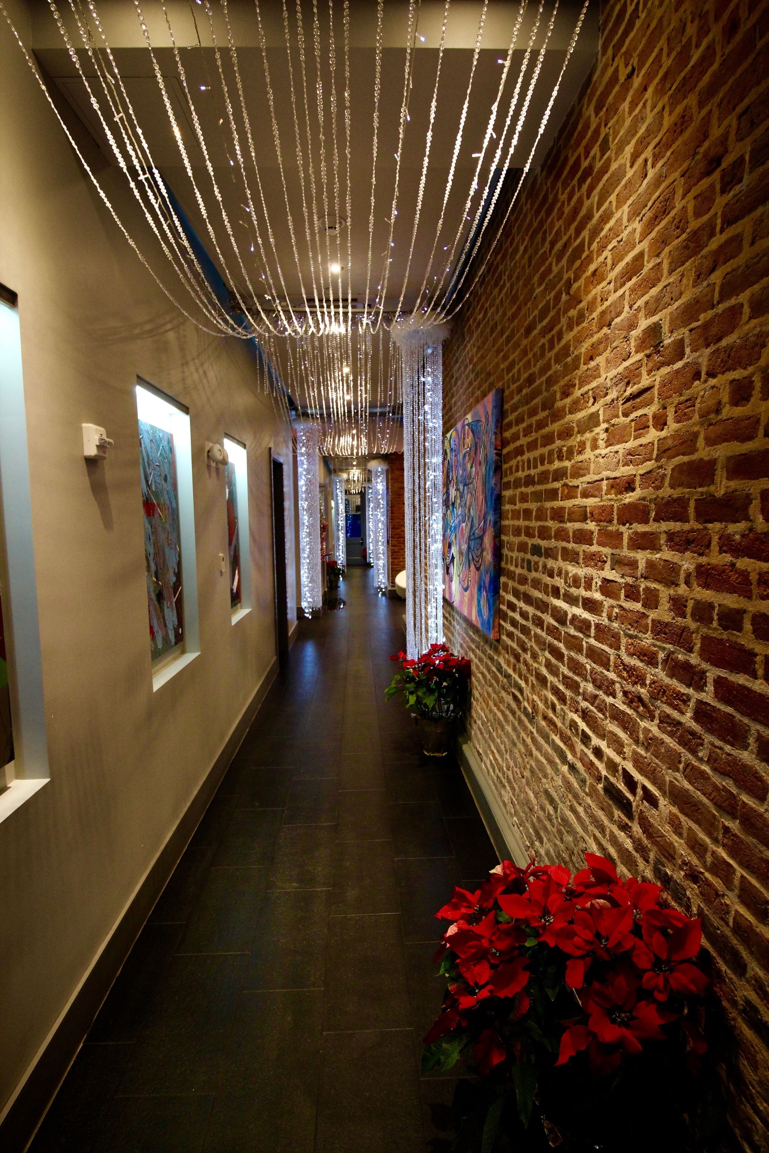 A hallway with a brick wall, artwork, and a plant with red flowers.
