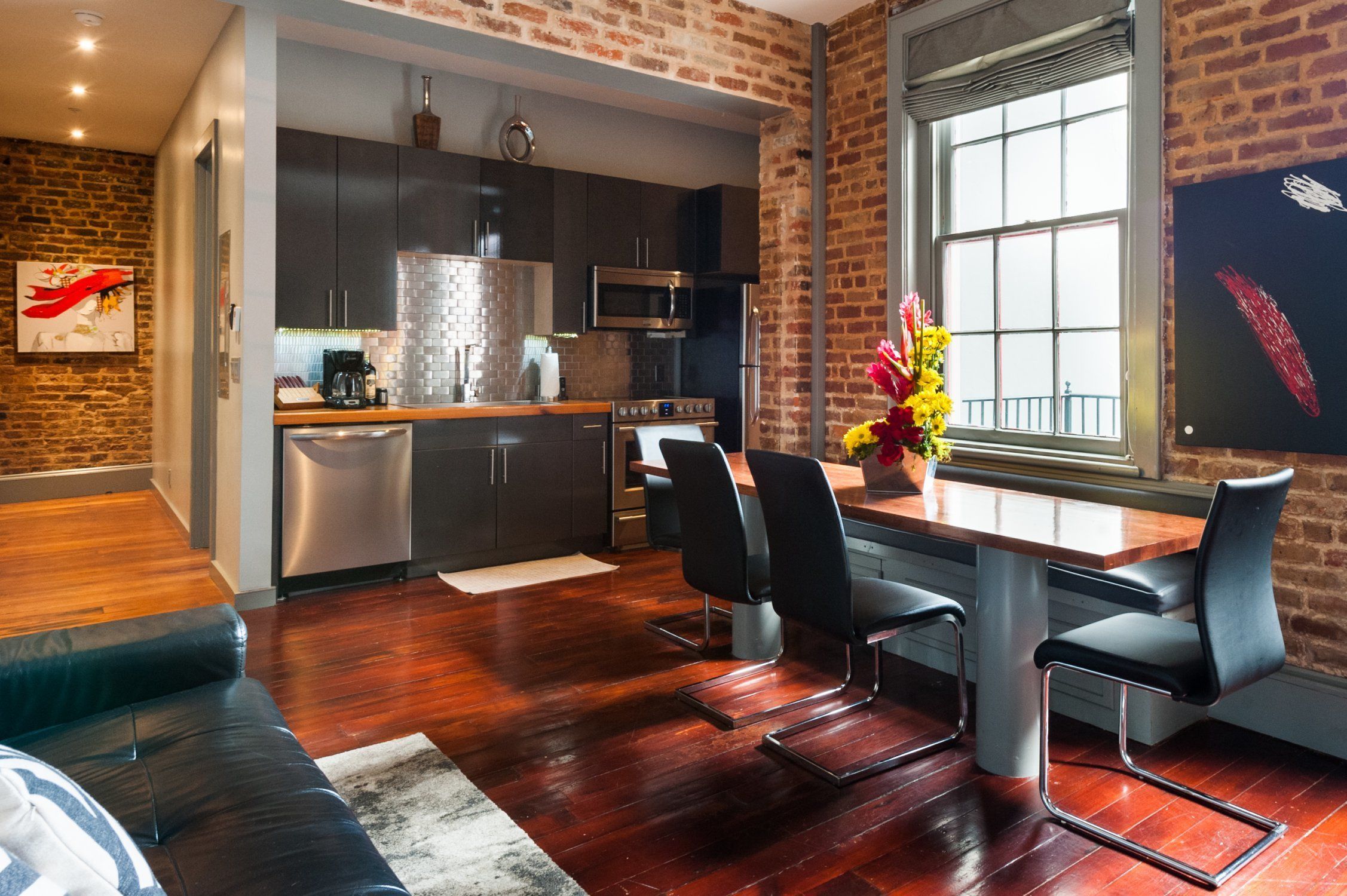 A modern kitchen with dark cabinets, stainless steel appliances, and a brick wall.