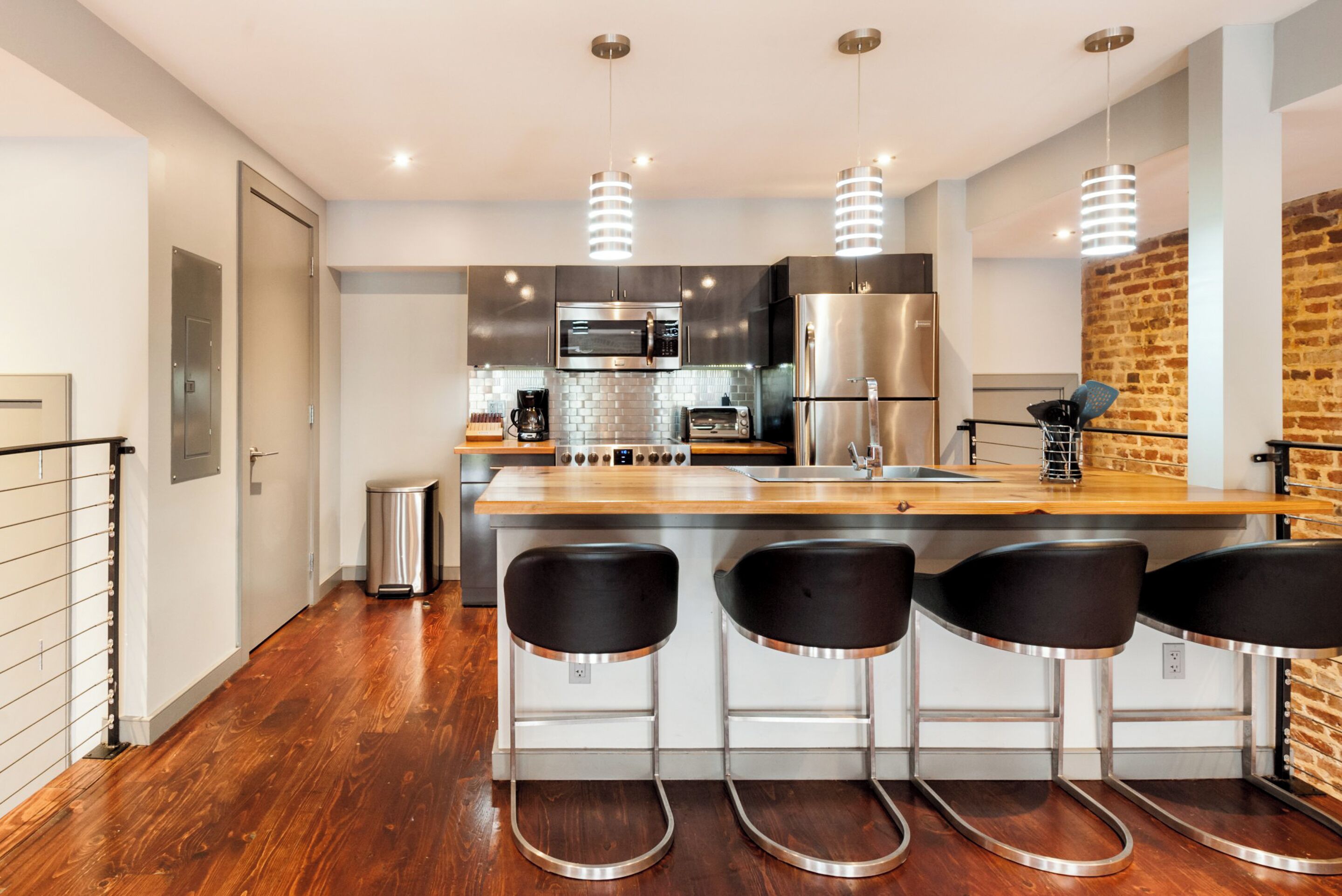 Una cocina moderna con electrodomésticos de acero inoxidable, encimera de madera y tres taburetes negros.