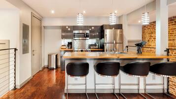 Una cocina moderna con electrodomésticos de acero inoxidable, encimera de madera y tres taburetes negros.
