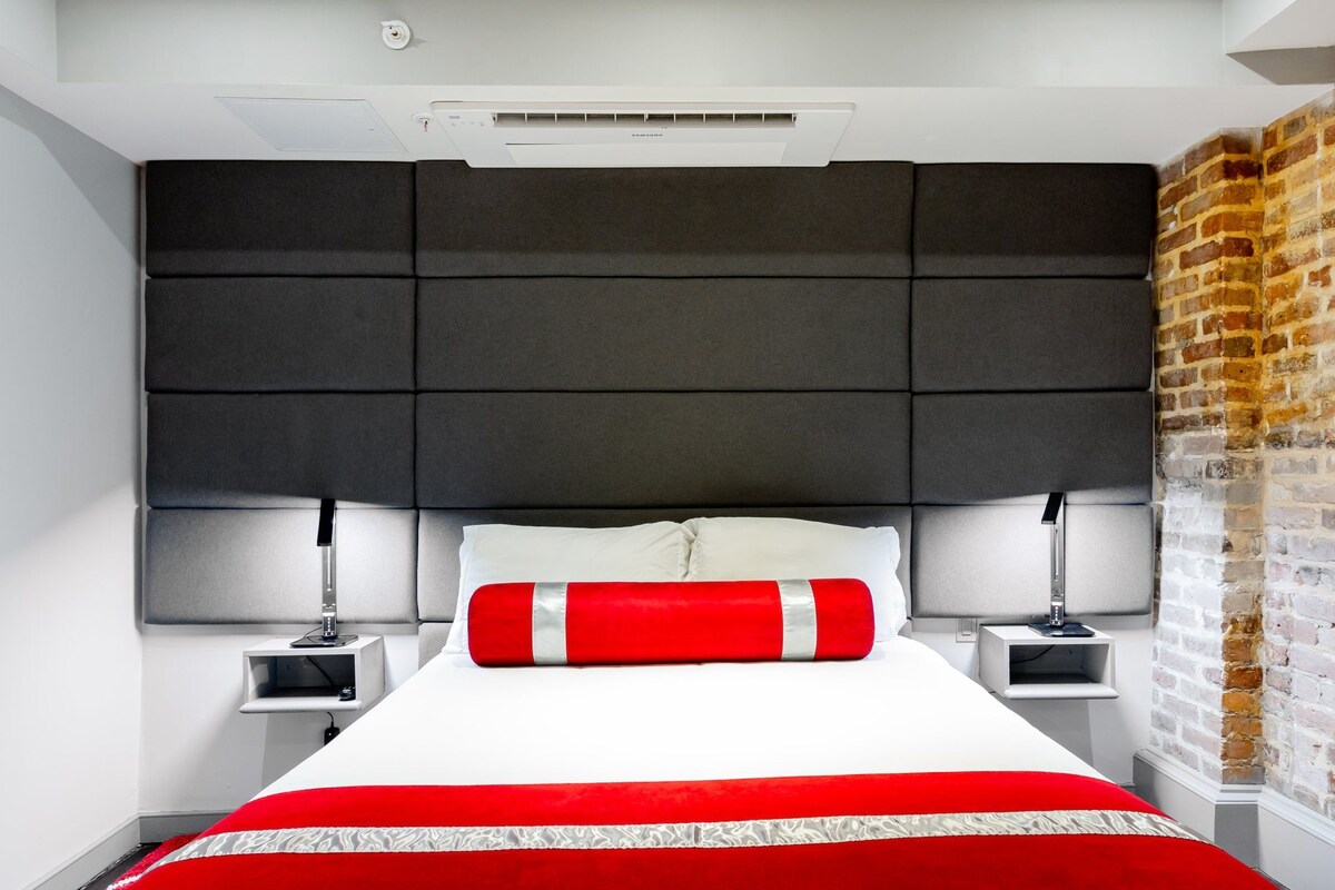 A modern bedroom with a large bed, a headboard with storage compartments, and a brick wall accent.