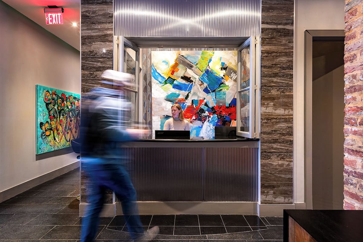 A modern elevator with a glass enclosure, a visible exit sign, and a textured wall.