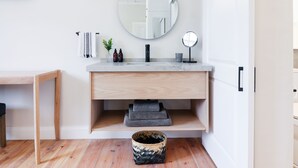 Un baño moderno con tocador de madera, un espejo redondo y un lavamanos pequeño.