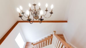 Una escalera con barandas de madera y un candelabro con múltiples luces.