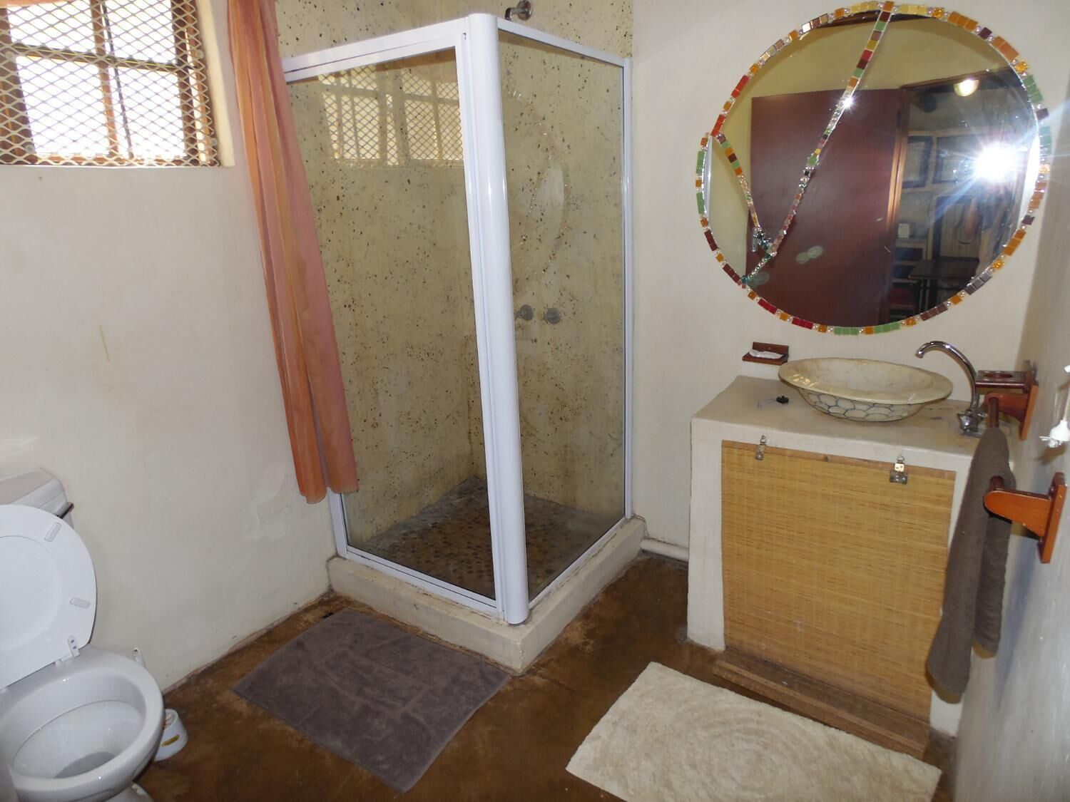 Un baño con cabina de ducha, inodoro, lavabo con espejo de mosaicos y un mueble pequeño.