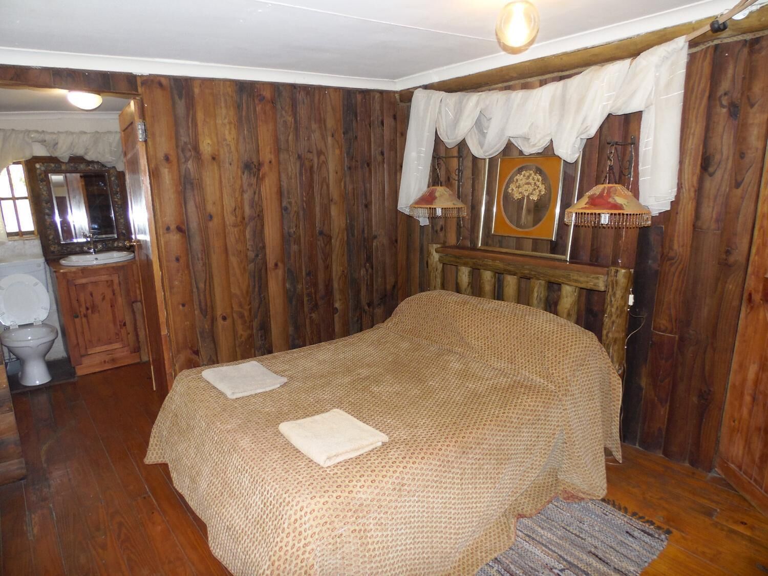 A wooden-paneled bedroom with a bed, a wooden headboard, a nightstand, a lamp, and a mirror.