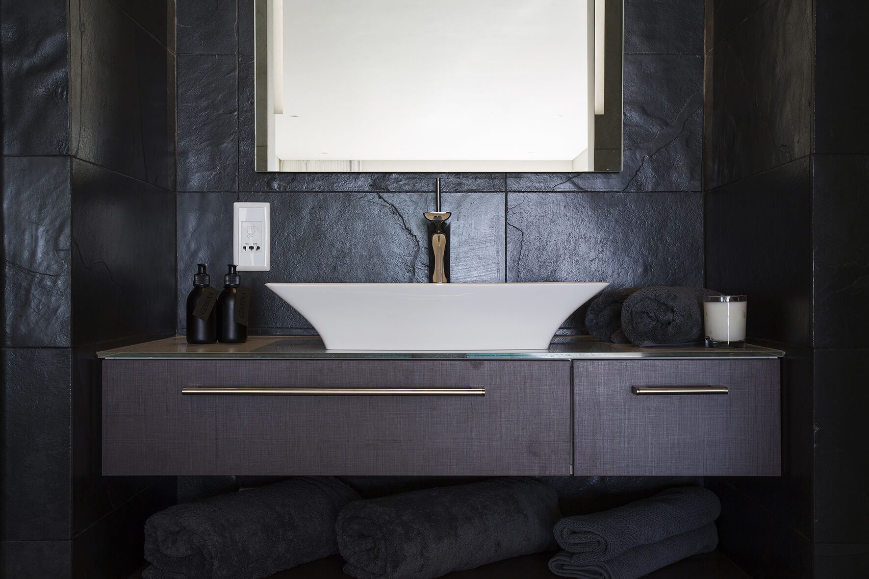 Une salle de bain dotée d’un lavabo moderne, de carreaux foncés et d’un porte-serviettes.