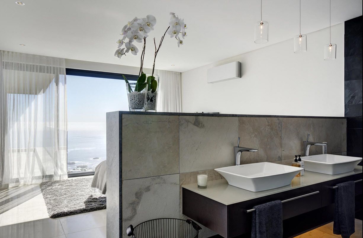 A modern bathroom with two sinks, a large mirror, and a view of the ocean.