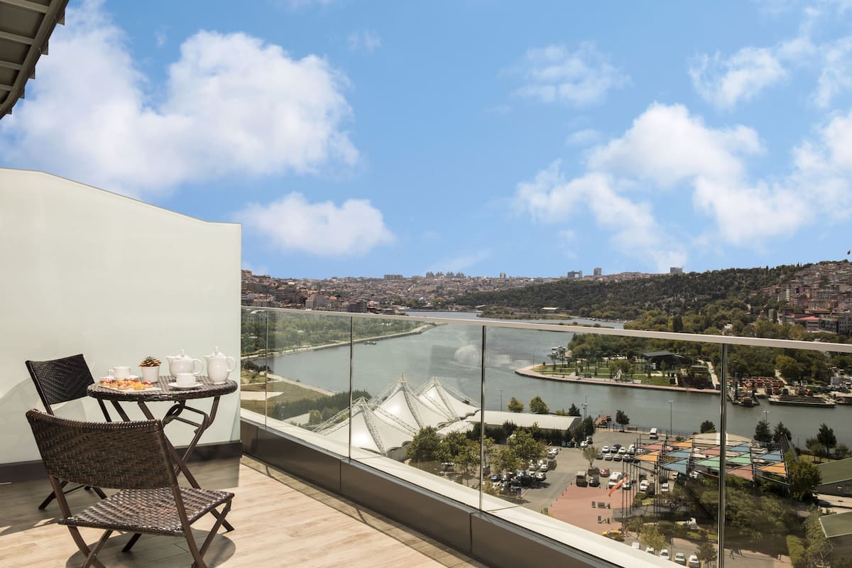 A balcony with wicker chairs and a table, overlooking a river and cityscape.