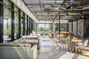 A modern restaurant with large windows, geometric patterned flooring, and a variety of seating arrangements including tables and sofas. - Arise Hotel Golden Horn (Istanbul)