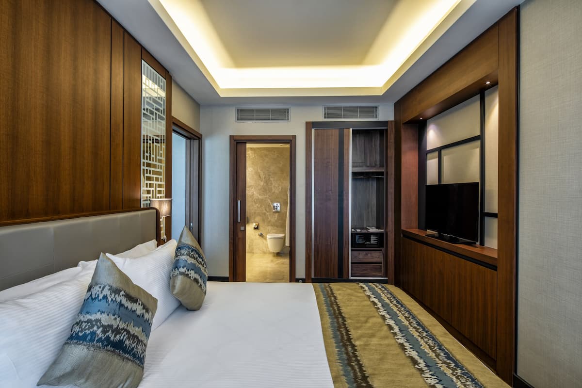 A modern hotel room with a large bed, a television, a wardrobe, and a bathroom visible through an open door.