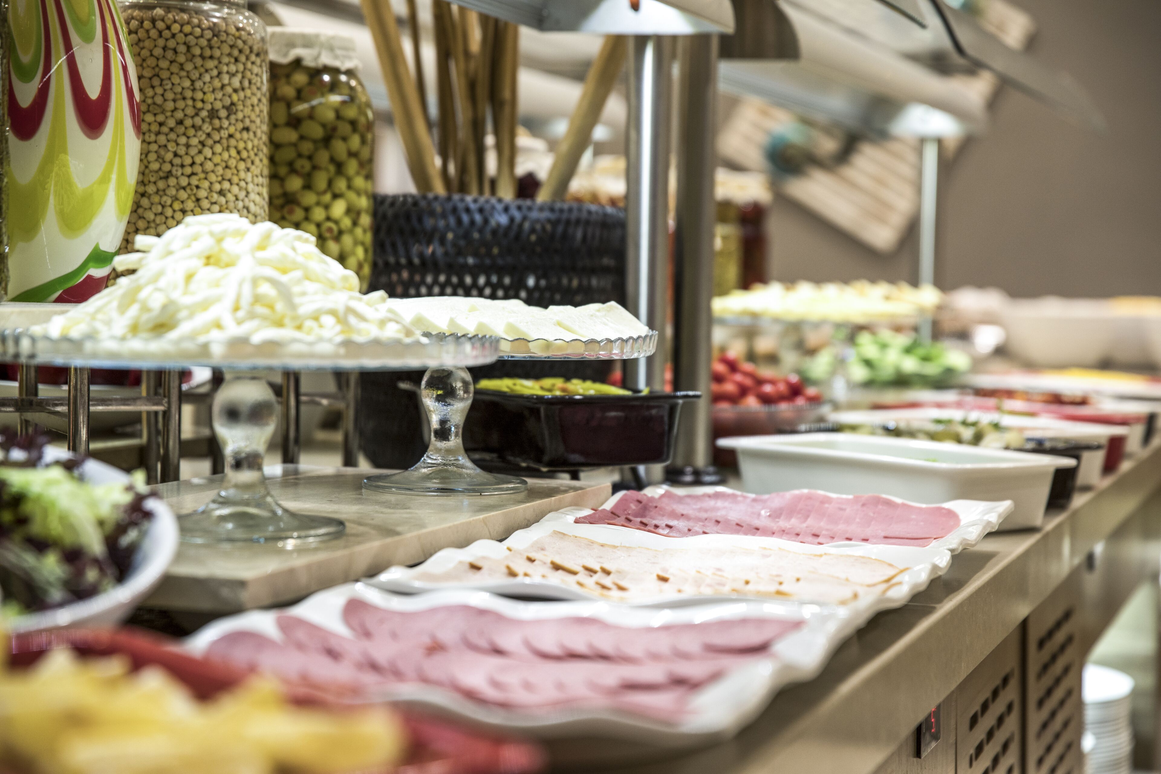 Un bufé con diversas opciones de comida, incluyendo ensaladas, quesos y carnes.
