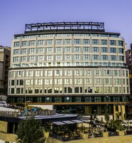 Un hotel de varios pisos con un diseño moderno, que cuenta con un espacio exterior cubierto con asientos y un parque infantil.