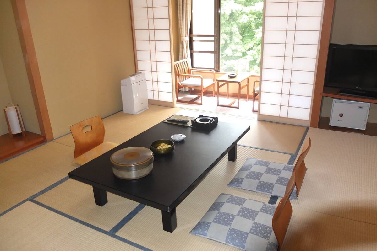 Perinteinen japanilainen huone, jossa on tatamimatto, matala pöytä, jossa on kulho ja kuppi, sekä televisio, joka on sijoitettu kaappiin.