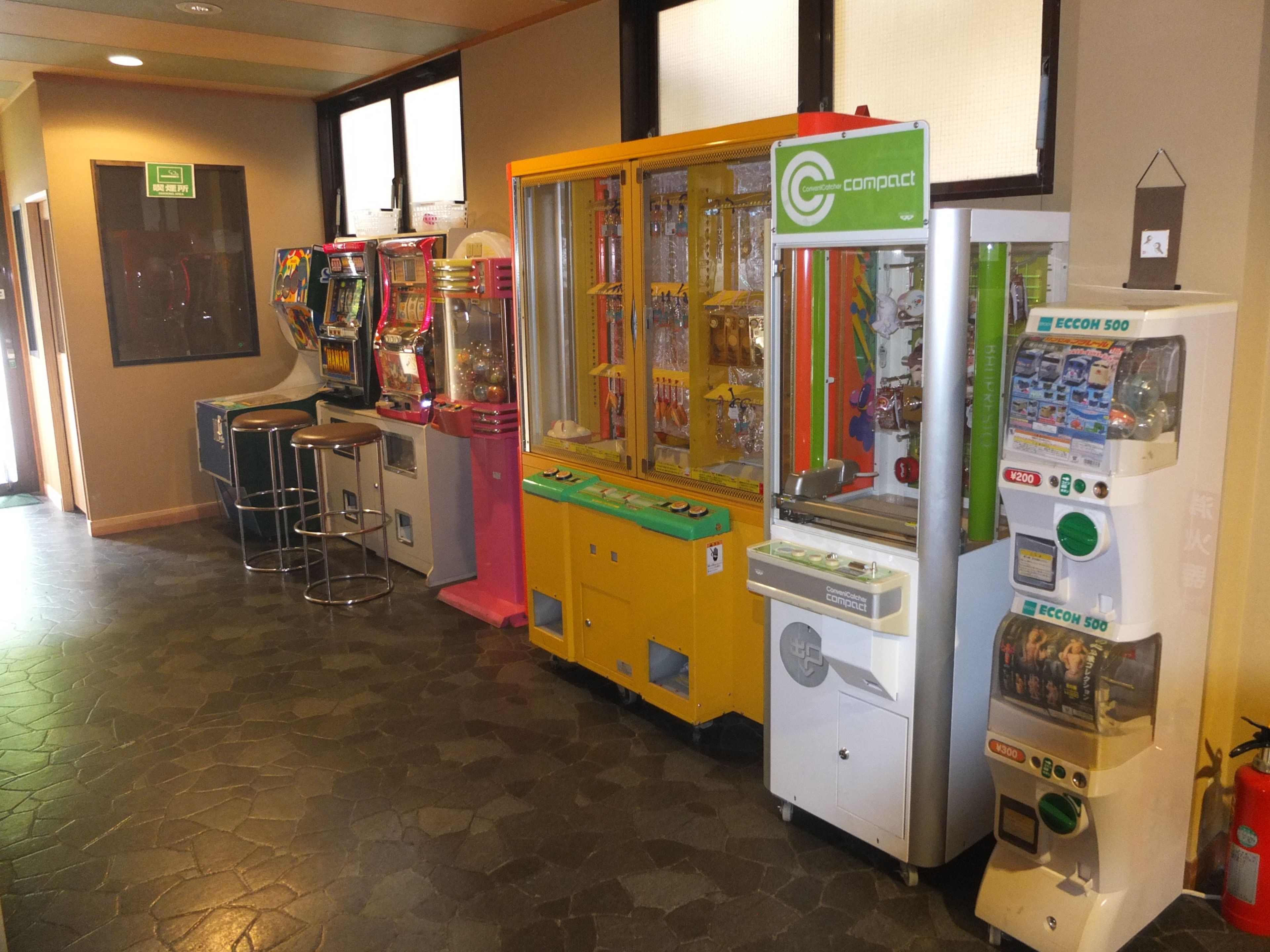 A row of arcade machines in a room with a tiled floor and a window in the background.