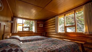 A cabin room with two beds, wooden walls, large windows, and a bench. - Northern Rockies Lodge (Muncho Lake)