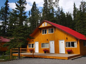 A wooden cabin with a red roof, two doors, and a porch with potted plants.