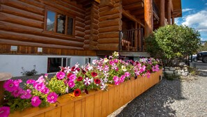 A wooden log cabin with a balcony and a flower bed with pink and red flowers. - Northern Rockies Lodge (Muncho Lake)