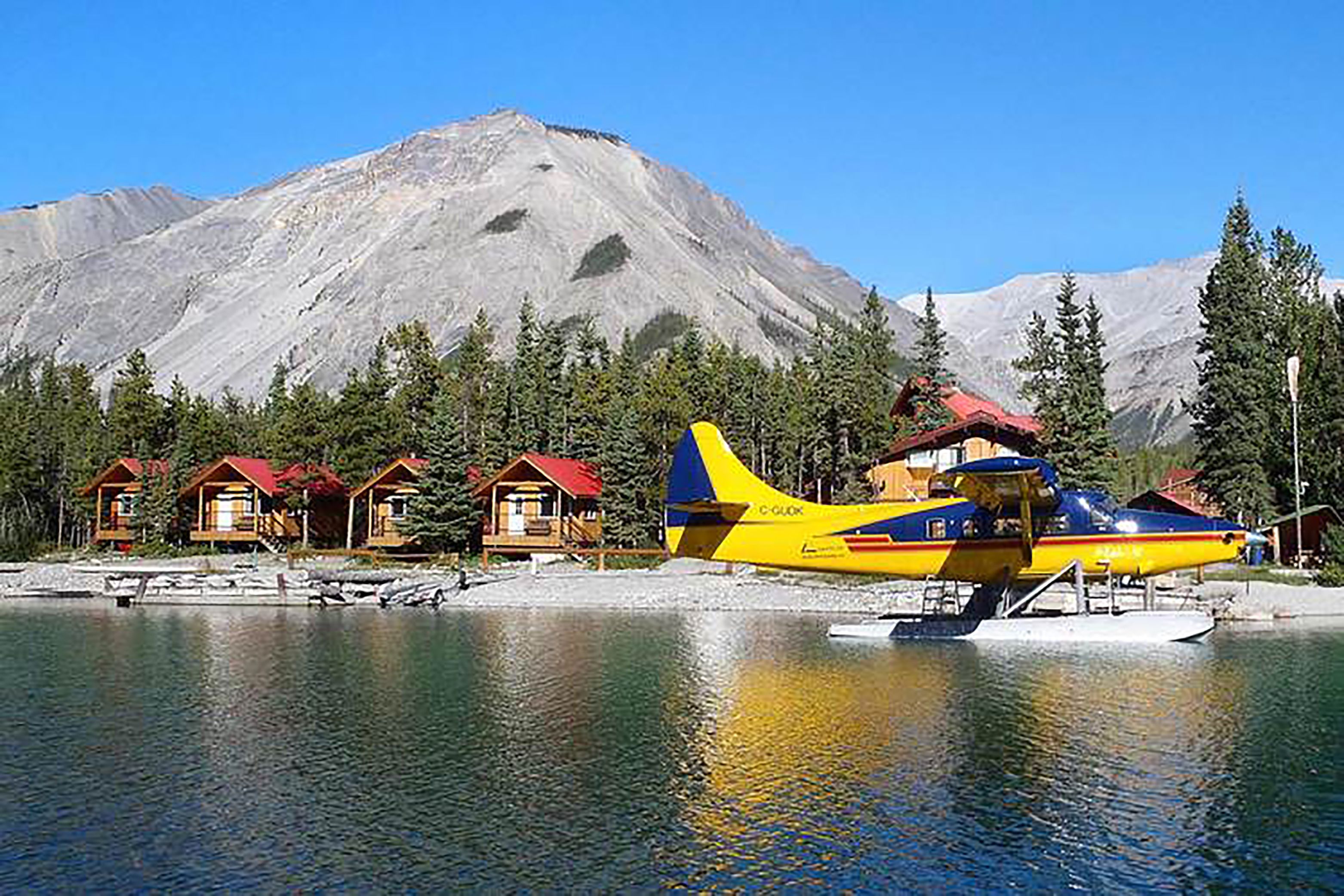 A yellow and blue seaplane parked by a lake with cabins in the background.
