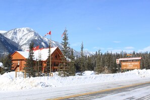 A wooden lodge with a sign for Northern Rockies Lodge, a road with snow, and a mountain in the background.