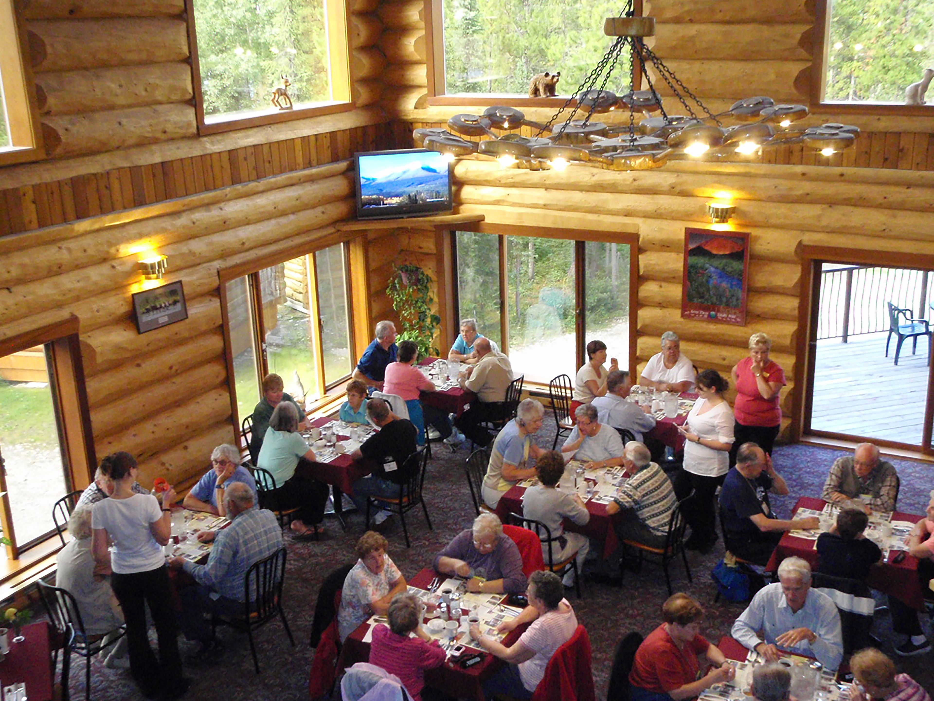 A log cabin restaurant with wooden walls and large windows. Tables are set for dining, and people are seated.