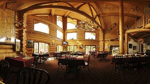 A log cabin with multiple dining areas, a large map on the wall, and a stone fireplace. - Northern Rockies Lodge (Muncho Lake)